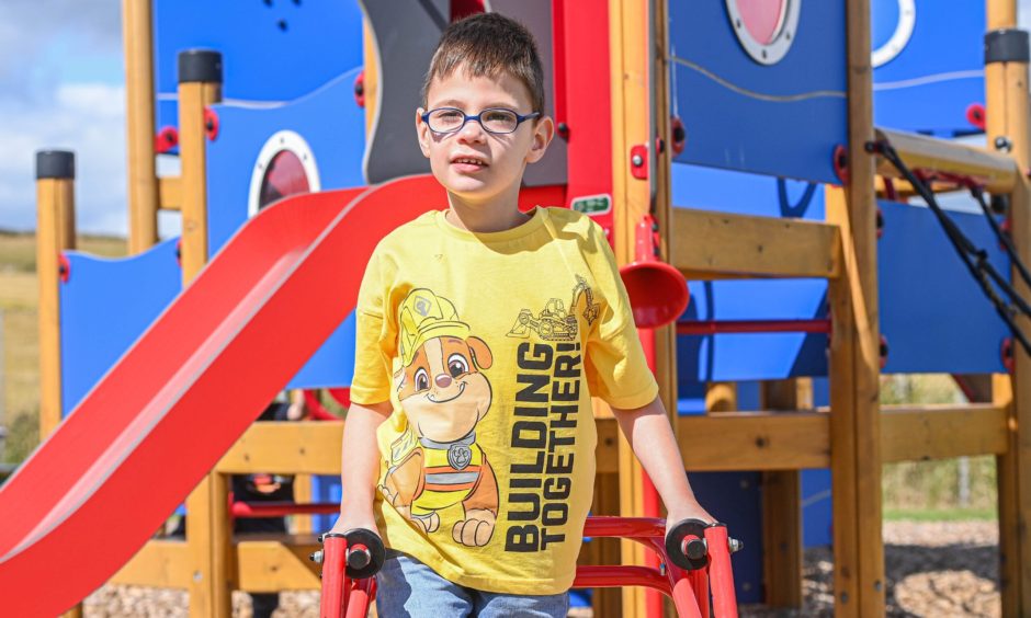 Harrison in a play park using his walking frame.