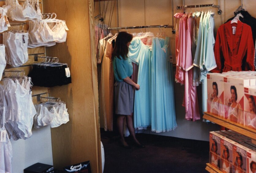 A shop assistant shows off a rail of women's clothing.