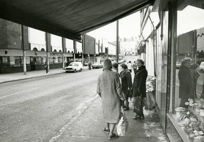 People on the pavement outside a shop, looking across at the Lowfreeze and Boots store.