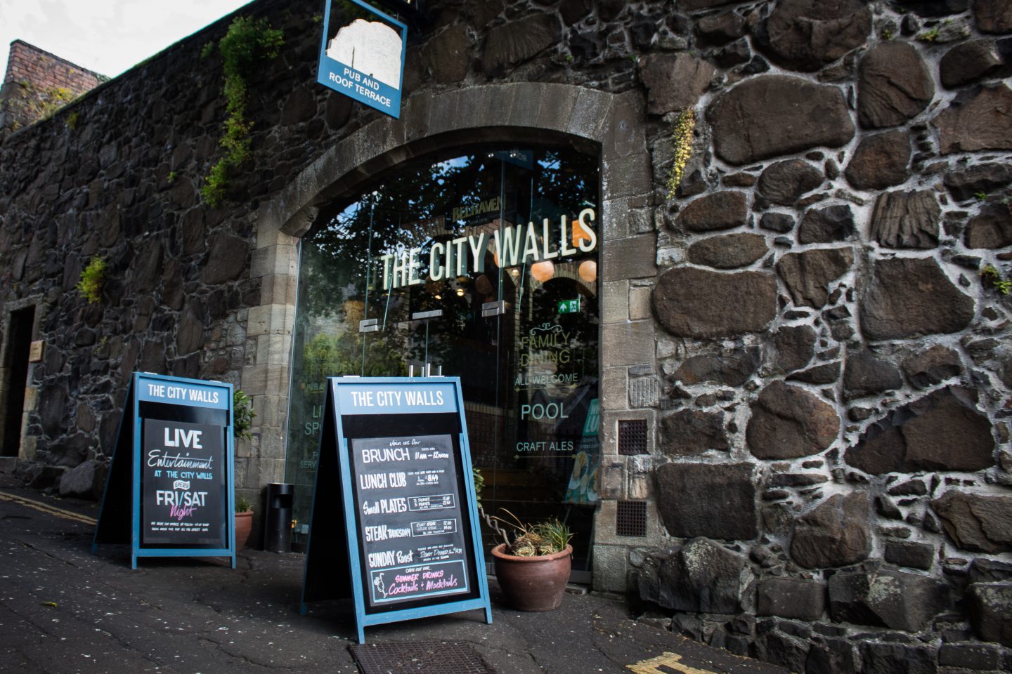 Old wall with a glass doorway and a sign saying "The City Walls". 