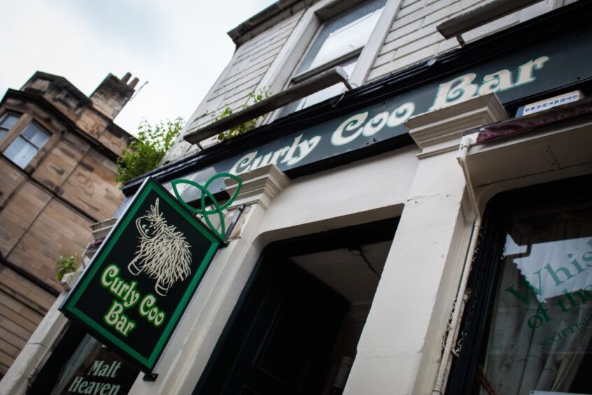 Green sign saying "Curly Coo Bar" with a picture of a cow. 