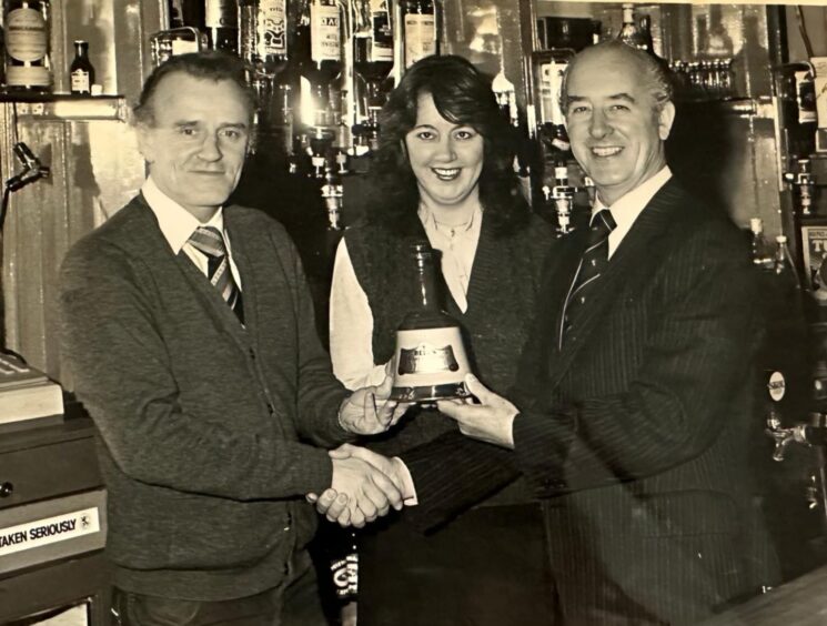 Joe and Joan Roberts receive a decanter of Bells from Bill Beattie of Bells. Image: Supplied.