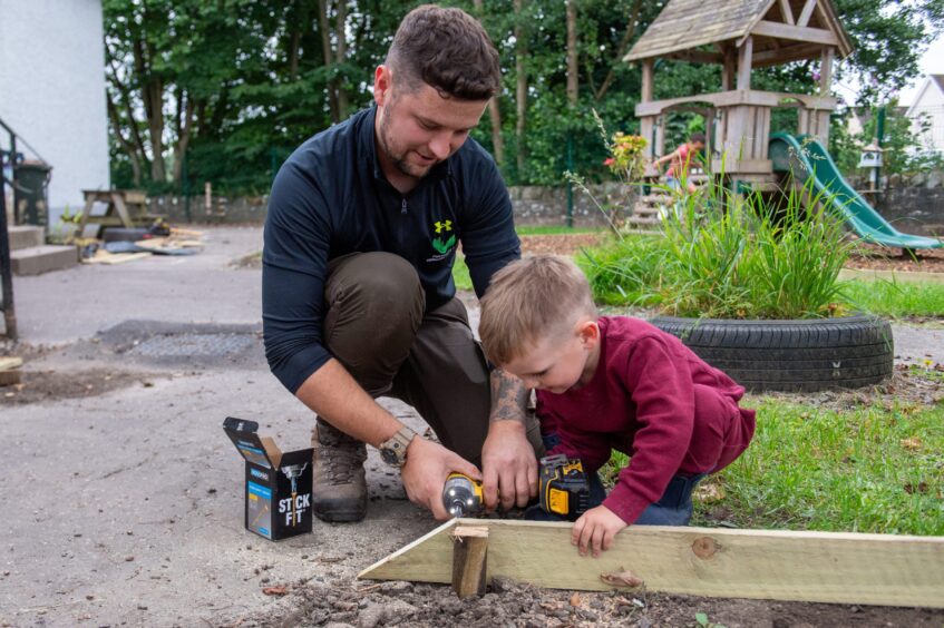 Connor Park kneeling working on timber edging at Auchtergaven nursery, with son Albie holding piece of wood