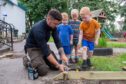 Connor Park on his knees working in outdoor classroom helped by three small boys