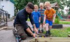 Connor Park on his knees working in outdoor classroom helped by three small boys