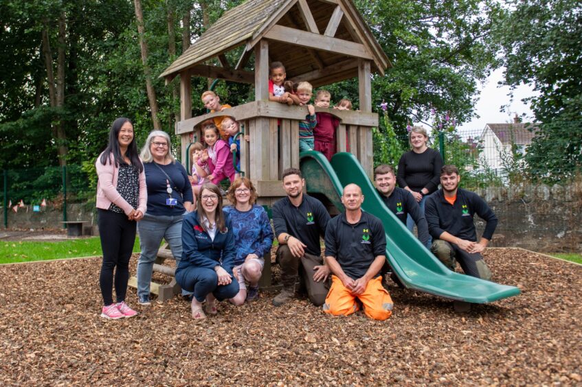 Group of people standing around climbing frame and slide in outdoor classroom at Auchtergaven nursery