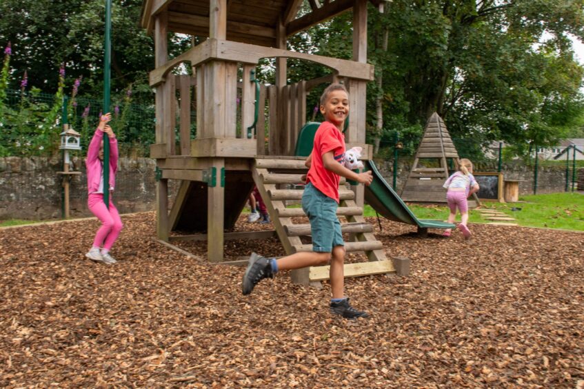 Children playing on bark covered surface next to timber climbing frame at Auchtergaven school