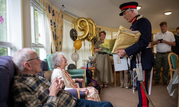 Lord Lieutenant Robert Balfour presents Jean Grossett with her BEM, watched by husband John