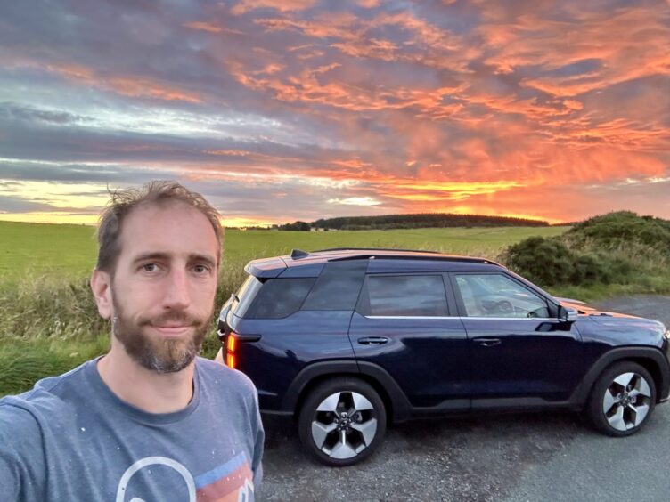 Jack beside the KGM Torres EVX in the Fife countryside at sunset