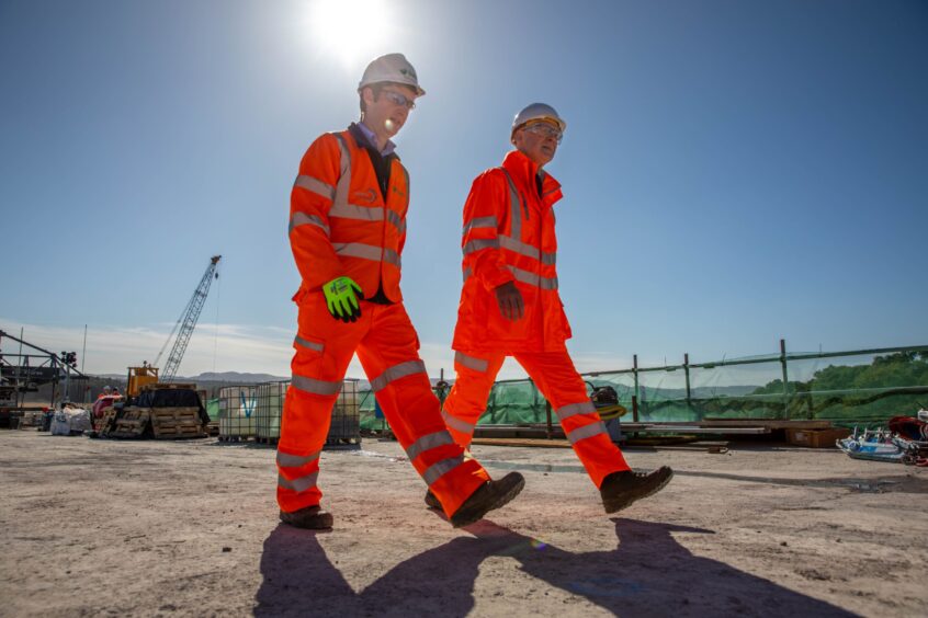 John Swinney and Derek Walsh in orange high vis suits, walking across Destiny Bridge