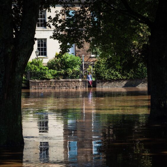 Person standing at gate of Marshall Place home in Perth, looking out at floodwater in front of them