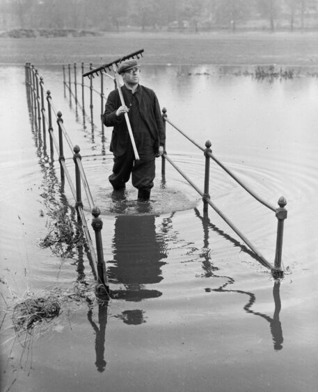 Black and white photo of man wading through knee deep floodwater somewhere in perthshire