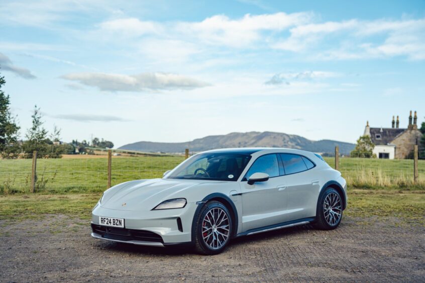 the car with fields, hills and a cottage in the background