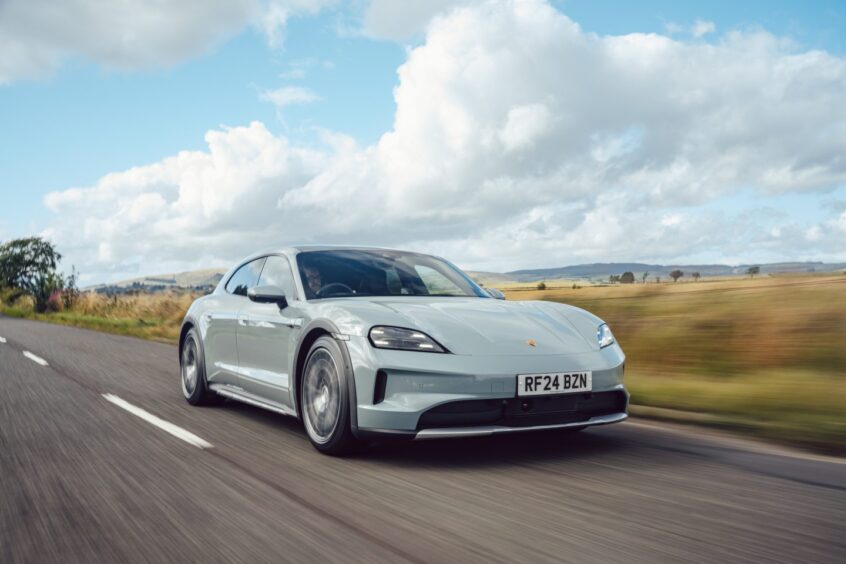 the Porsche Taycan Cross Turismo on the road with a field in the background