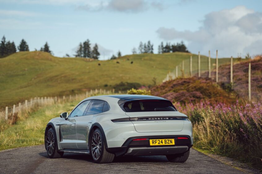 The Porsche Taycan Cross Turismo seen from the rear on a country road with fields all around