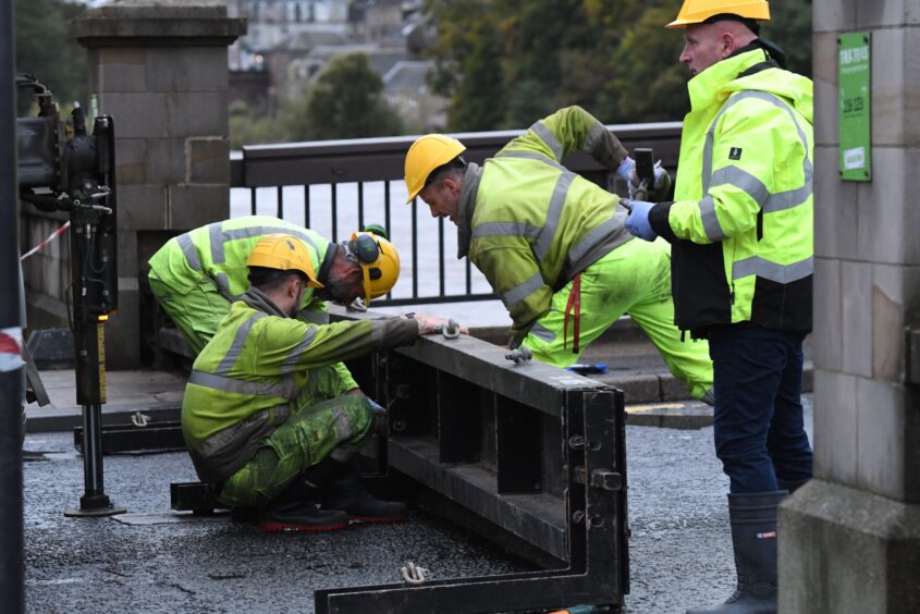 Group of workers in high vis gear moving heavy floodgates parts into place beside River Tay in Perth