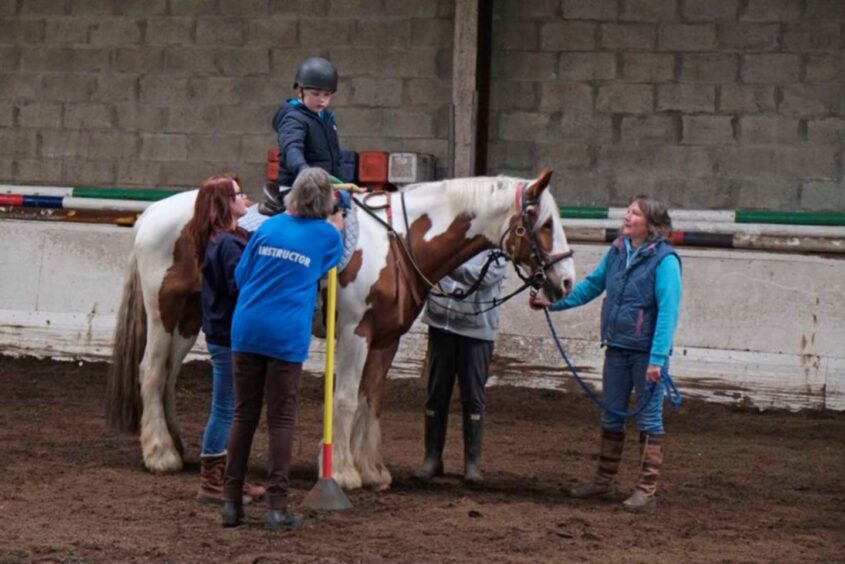 Youngster on horseback with group of RDA volunteers around him