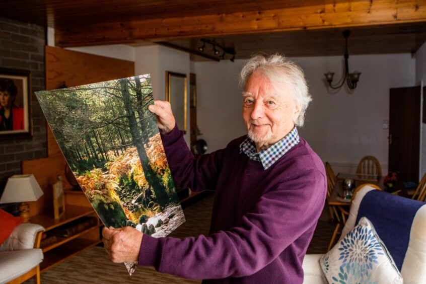 A smiling Alex Coupar holds up one of his photographs, a nature scene