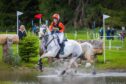 Person on white horse riding across water obstacle