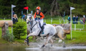 Person on white horse riding across water obstacle