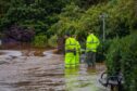 Men in yellow hi vis gear standing next to open flood gate as filthy brown water pours through from River Tay