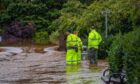 Men in yellow hi vis gear standing next to open flood gate as filthy brown water pours through from River Tay