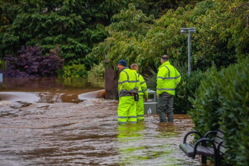 Three workers in yellow high vis gear knee-deep in floodwater in a Perth park