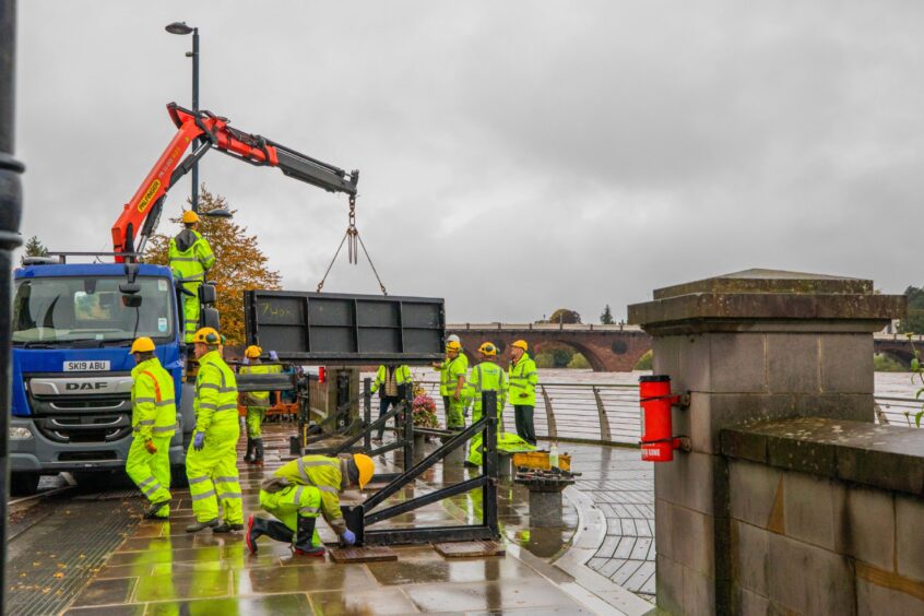 Lorry delivering heavy metal flood gates to crew of workers in high vis suits beside River Tay in Perth