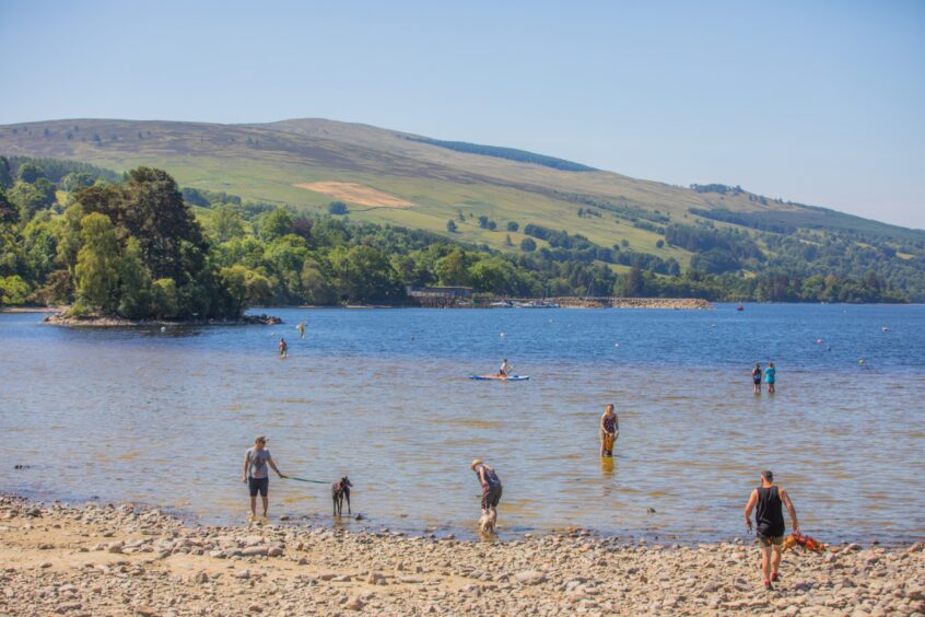 Loch Tay with beach in foreground and people padding and swimming in the water on a sunny day