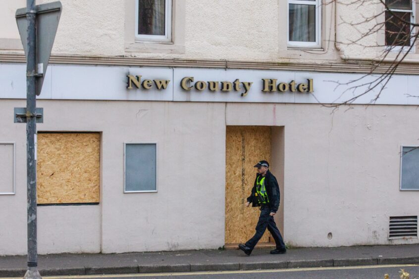 Police officer walking past boarded doors and windows of County Hotel, Perth