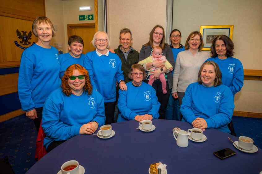 Group of Glenfarg Riding for Disabled volunteers in matching blue sweatshirts, seated and standing around a table in a function suite