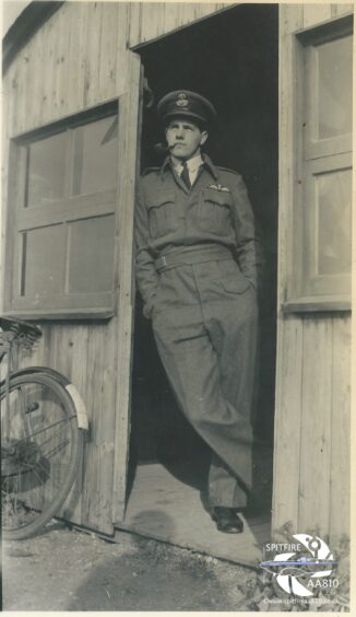 Black and white photo of Sandy Gun in RAF uniform leaning against door and smoking pipe