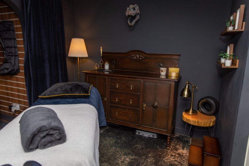 Death's Door sports massage treatment room, painted black with large animal skull on wall and heavy old furniture with candles and brass lamps.