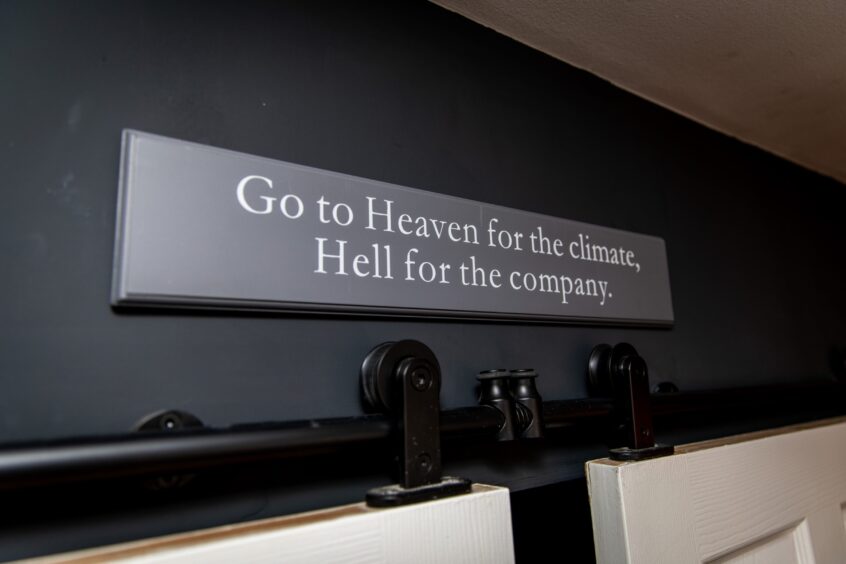 Sign which reads 'Go to Heaven for the climate, Hell for the company' on black painted wall at Deaths Door Sports Massage