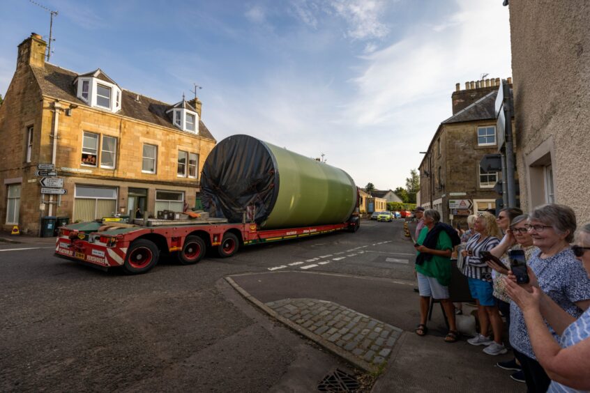 Group of women taking photos as lorry with large turbine tower on loader passes through Dunning