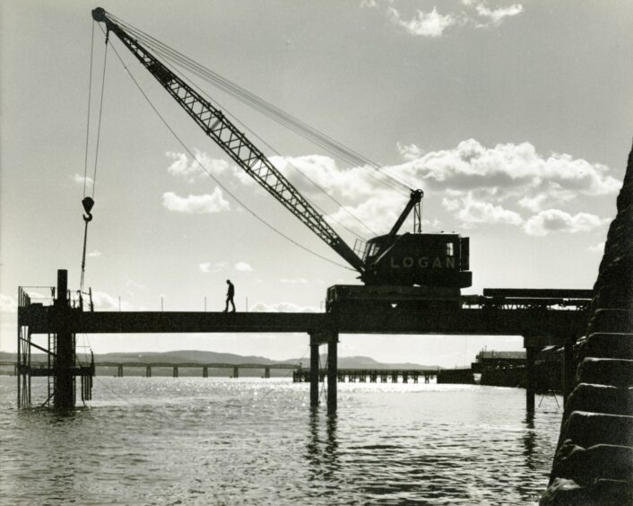 A man and some machinery in profile above the river as the bridge is built