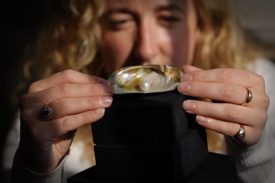 Woman holding pearl in shell up to camera
