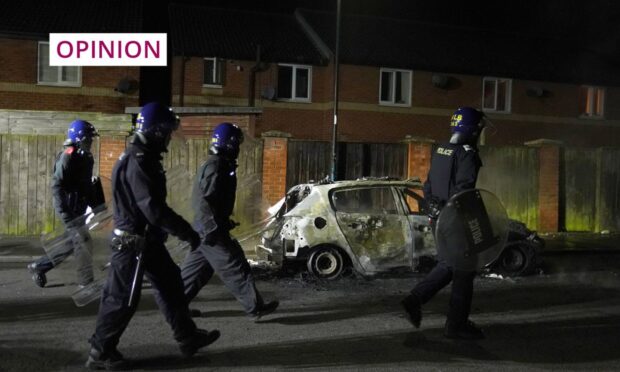 Riot police walk past a burnt out police vehicle as they are deployed to a violent protest in Hartlepool. Image: Owen Humphreys/PA Wire