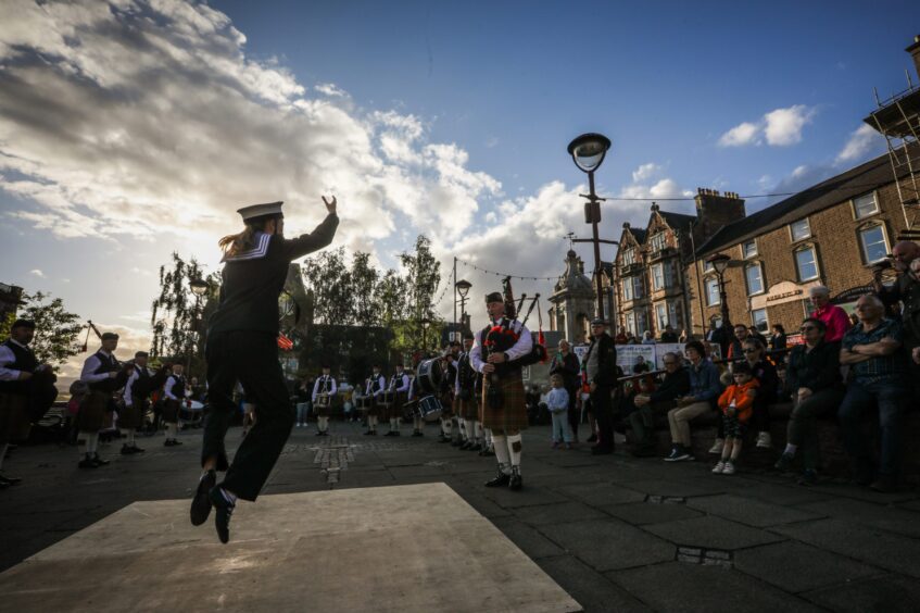 Dancer in sailor costume performing in front of fountain and pipe band in Crieff square