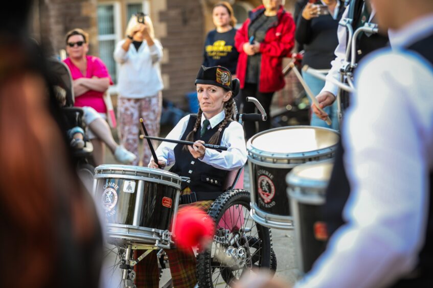 Comrie pipe band member in wheelchair playing drum watched by crowd