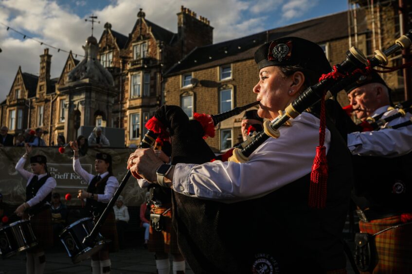 Pipe band members playing in front of Crieff fountain