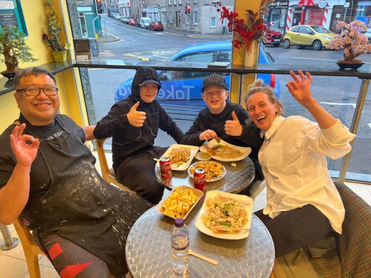 Pete seated at table in China China with woman with two young boys eating food and giving thumbs up