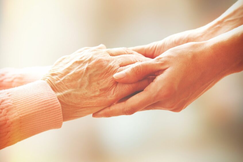 Younger pair of hands holding elderly person's hands