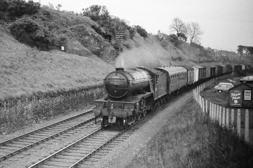 The southbound fish train going at speed in 1961 with a banking on one side and parked cars on the other