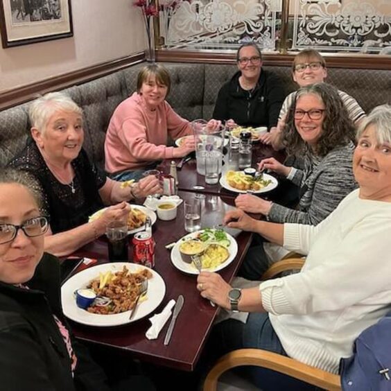 Group of seven women seated round pub table enjoying lunch