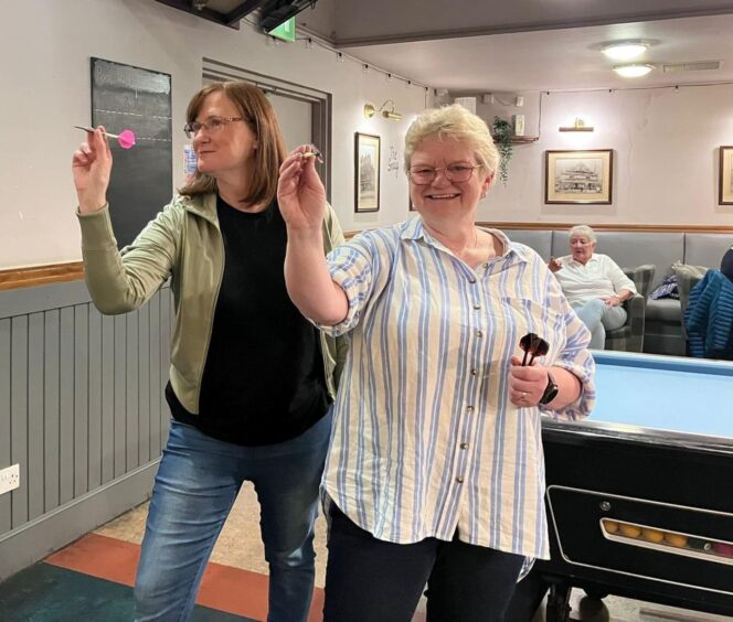 Two women taking aim at darts board