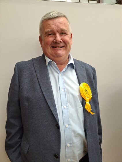 Alan Watt smiling in yellow Lib Dem rosette