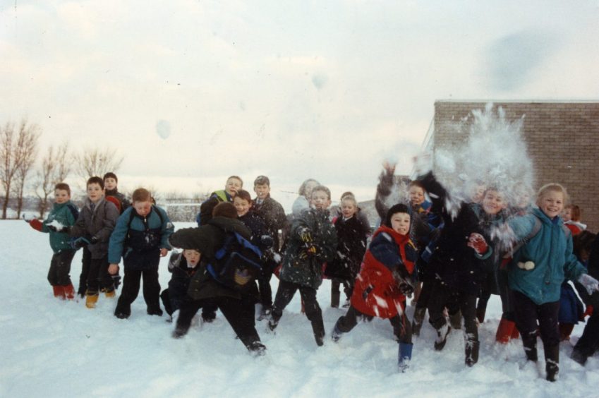 children in a school playground throw snowballs towards the camera