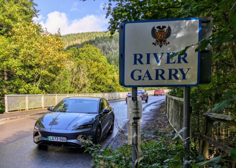 The BYD Seal on a bridge near Pitlochry, with a forest in the distance.