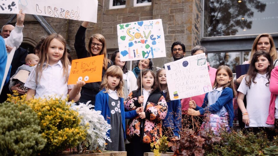 Group of adults and children with placards outside Birnam Library